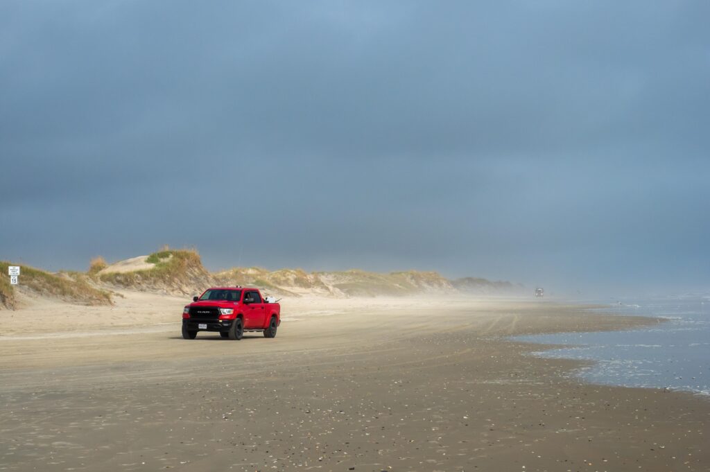 A red truck driving on the beach on a cloudy day north of Corolla North Carolina